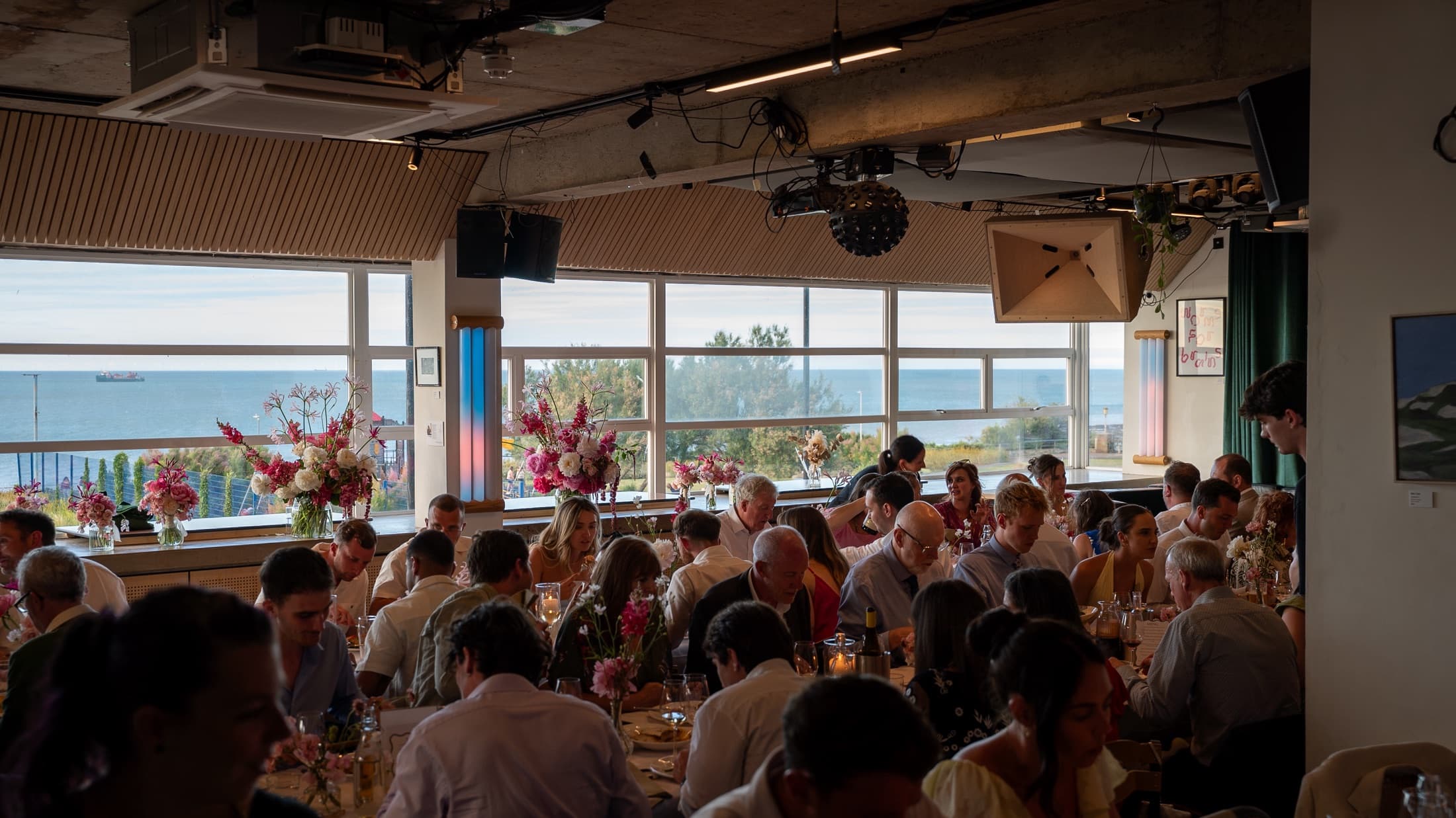 A wedding at Faith in Strangers: every table full, flowers on the tables, the sea behind